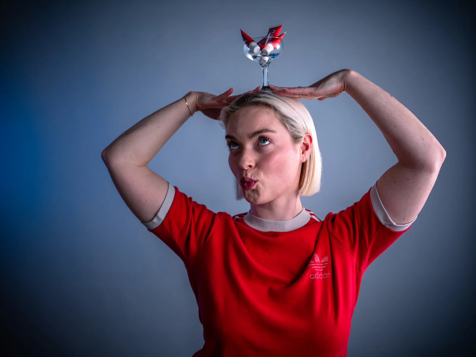 Lucy pouting, balancing a cocktail glass of CLUTCH Glue tubes on her head